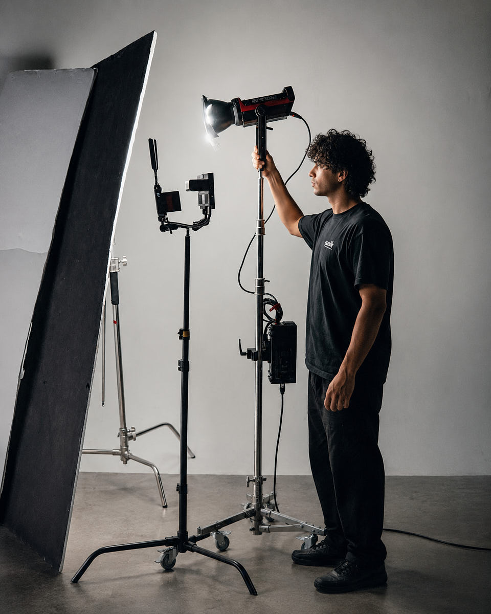 Lighting assistant standing beside a studio lighting setup with light stand, modifier, and grip equipment