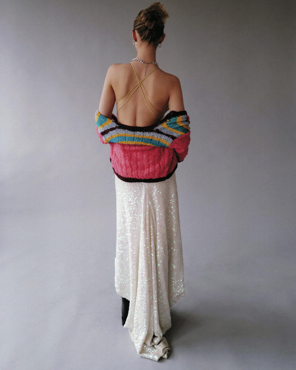 Back-view fashion lookbook image of a model wearing a colorful top and white pants