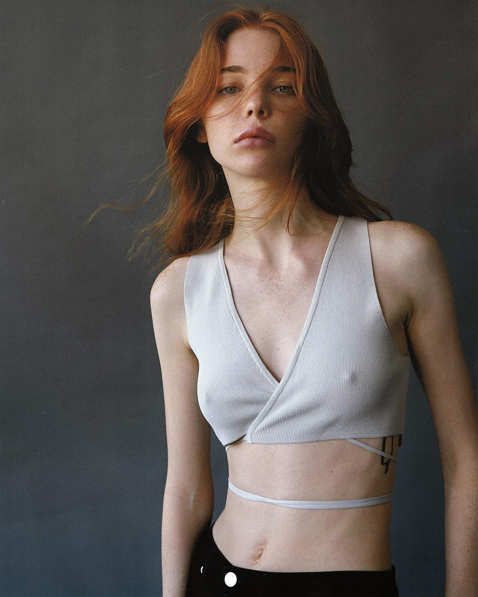 Editorial commercial portrait of a model in a cropped white top against a dark studio background