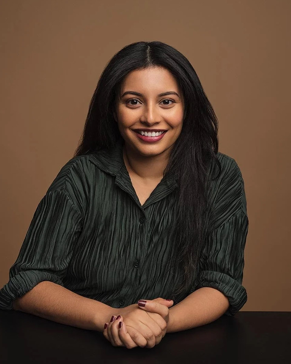 Seated studio headshot of a woman in a dark top against a warm neutral background