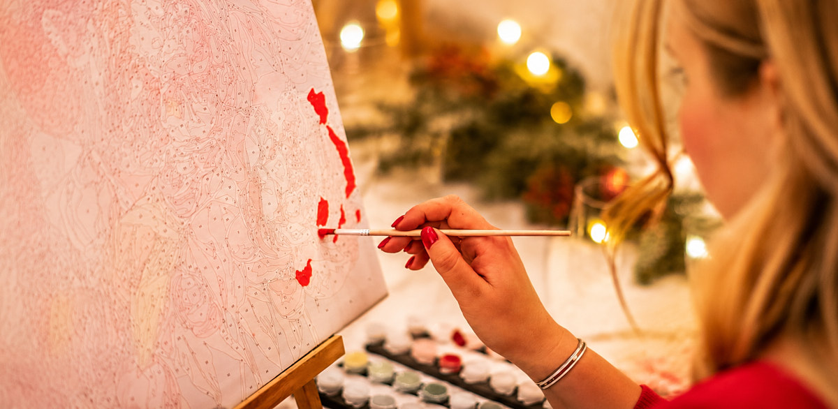 Close-up of a painting workshop participant working on canvas with warm decorative lights in the studio
